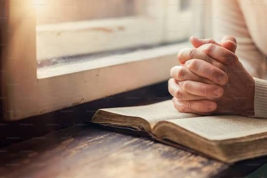 Hands folded in prayer over an open book